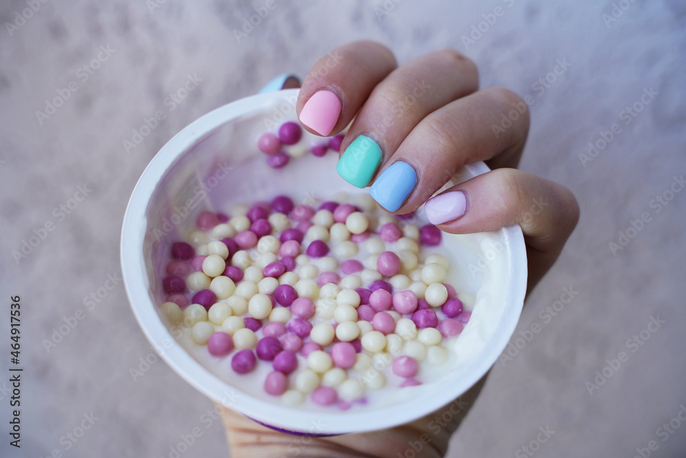 female hand with manicure different colors nails hold milk dessert with pink and white balls female hand with manicure different colors nails hold milk dessert with pink and white balls