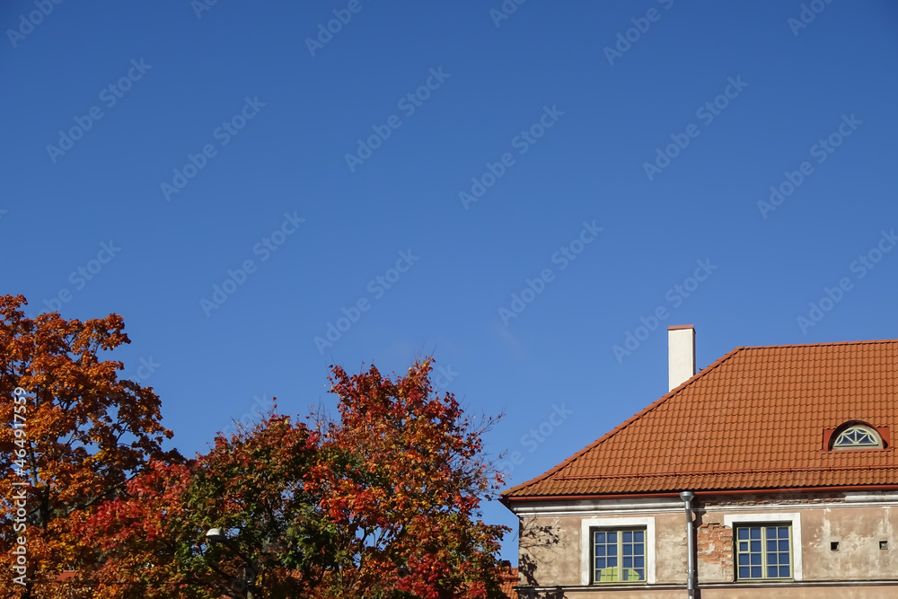 Close up of a house with red tiled roof. Cloudless clear blue sky background. Golden autumn tree foliage on the left. Autumn mood. Pelgulinna, Tallinn, Estonia, Europe. September 2021