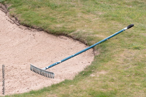 Close up of golf course sand bunker with a rake in the sand.