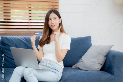 Young asian woman sitting thinking idea using credit card with laptop computer on couch, girl shopping online for buy and payment with notebook on sofa, finance and debit, lifestyle concept. © N_studio