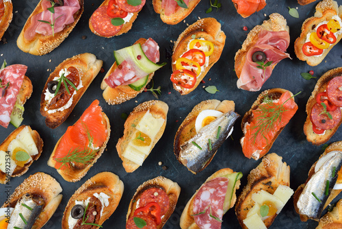 Delicious mixed Spanish tapas with typical specialties on roasted baguette with sesame on a dark background