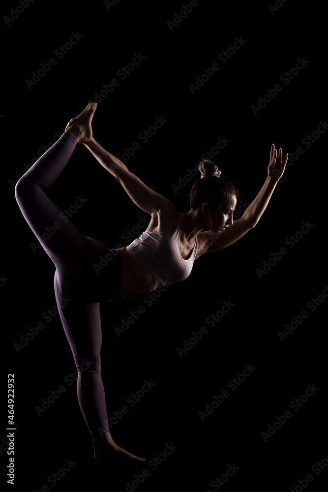 Fit girl practicing yoga in a studio. Half silhouette side lit fitness model.