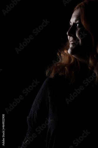 Portrait of a red haired woman against black background. Girl in shadows.