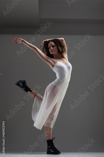 Girl with curly hair making ballet poses. Ballerina in white dress and black boots.