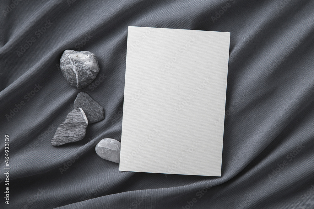 Fototapeta premium Blank greeting card on grey silk and decorating stones. Mockup.