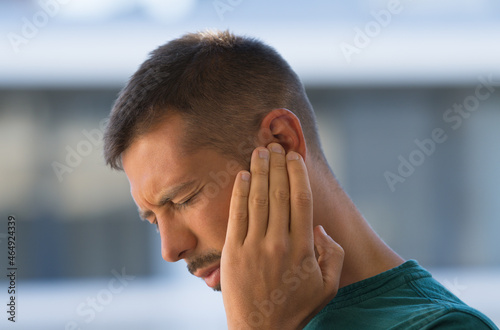 Young man with earache, otitis or tinnitus. Ear inflammation. Man suffering from ear pain photo