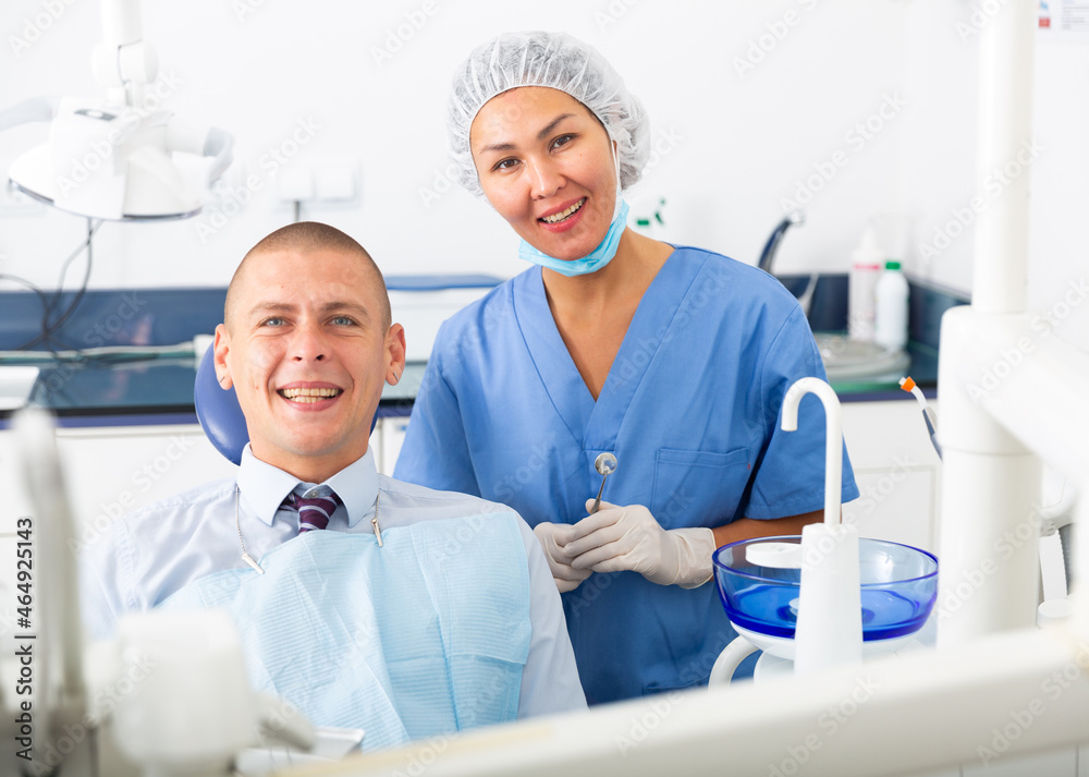 Portrait of a smiling asian woman dentist with a satisfied young man patient sitting in a dental chair in the clinic office