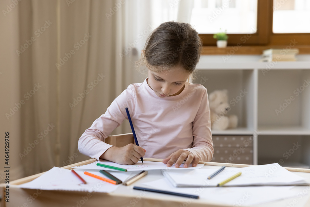 Focused adorable small preteen child girl drawing pictures with pencils on paper enjoying creative hobby activity, developing art skills sitting at table alone at home, art skills development. Focused adorable small preteen child girl drawing pictures with pencils on paper enjoying creative hobby activity, developing art skills sitting at table alone at home, art skills development.