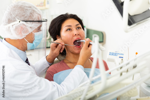 Dentist in face mask treating asian female patient using dental drill in dentist office