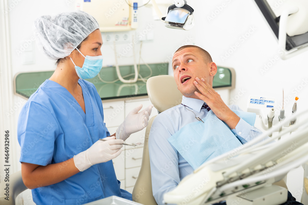 Obraz premium Young businessman complains of toothache to female dentist at dental clinic office