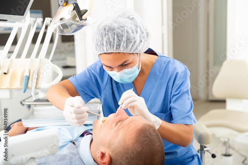 Dentist professional filling teeth for man patient sitting in medical chair