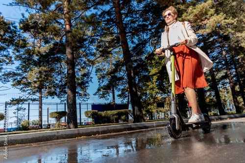 Middle aged adult woman rides an electric scooter in puddles. Leisurely lifestyle concept. Mental wellness.