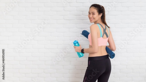 Asian beautiful women holding water bottle after play yoga and exercise on white brick wall background with copy space.Exercise for Lose weight, increase flexibility and tighten the shape.