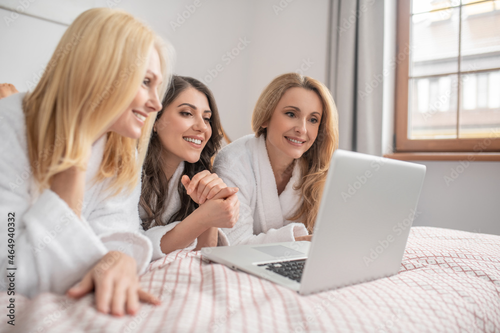 Smiling women looking at laptop screen on bed Smiling women looking at laptop screen on bed