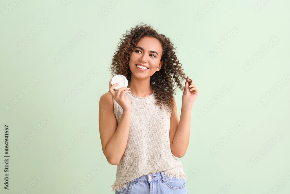 Young African-American woman with jar of cream on green background