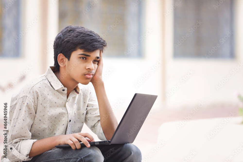 Indian stressed boy using a laptop while attending the online classes ...