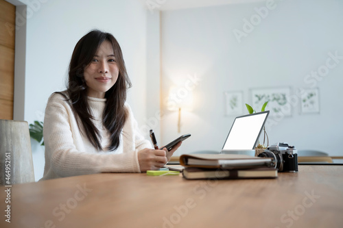 Charming asian woman holding smart phone and smiling to camera.