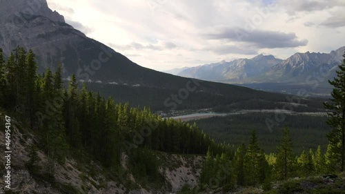 4K bird view footage of treetops of Kananaskis Country woods in the Canadian Rockies from above. Trekking in Canada and nature concepts. Young man hiking up a steep rocky slope taking in the view. photo