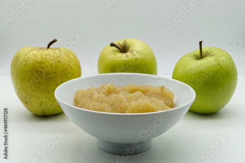 Apple sauce in a white bowl with raw apples on background. Apple puree and fresh green apples isolated on white background.