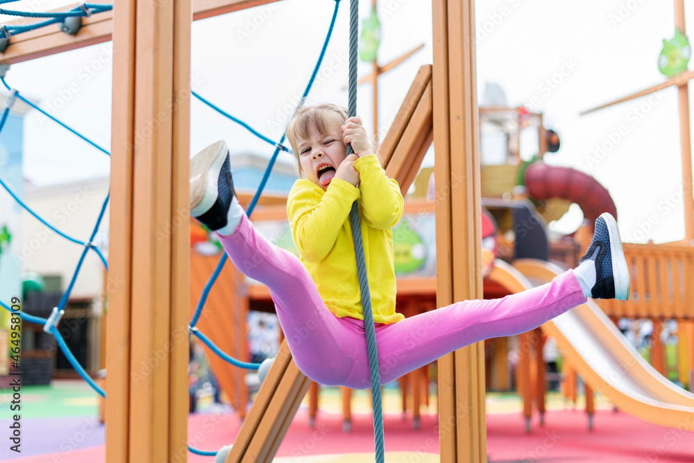 Fototapeta premium Cute little child girl having fun trying to climb on jungle gym at indoor playground, Physical, Hand and Eye Coordination, Sensory, Motor Skills development concept