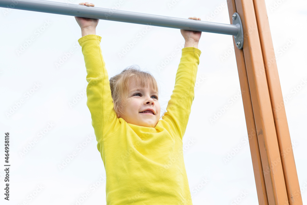 Fototapeta premium active little girl hanging on a horizontal bar in an open playground