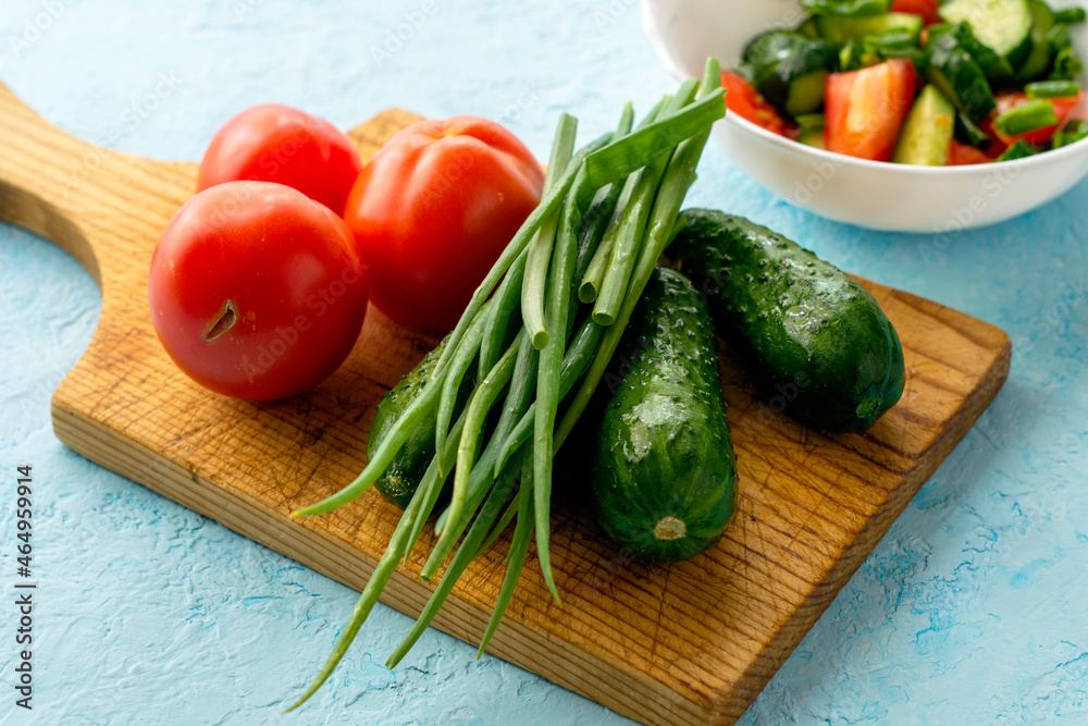 a cutting board with vegetables and a salad of cucumbers and tomatoes in a white bowl in the background a cutting board with vegetables and a salad of cucumbers and tomatoes in a white bowl in the background