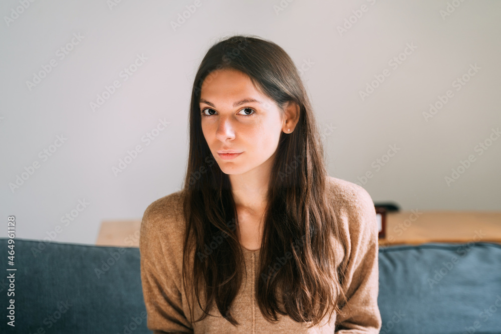 Millennial young pretty woman at home sitting on the couch. Confident and healthy portrait. Long brown hair and big eyes beautiful woman Millennial young pretty woman at home sitting on the couch. Confident and healthy portrait. Long brown hair and big eyes beautiful woman