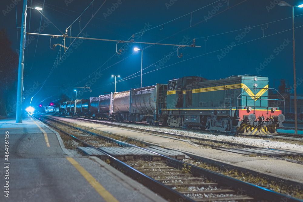 Fototapeta premium Green diesel train waiting to haul a train with tank cars into the night.