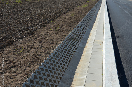 on the side of the road there is a concrete wall support and a ditch reinforced with perforated tiles. drains and drains away rainwater from the road and from the field.