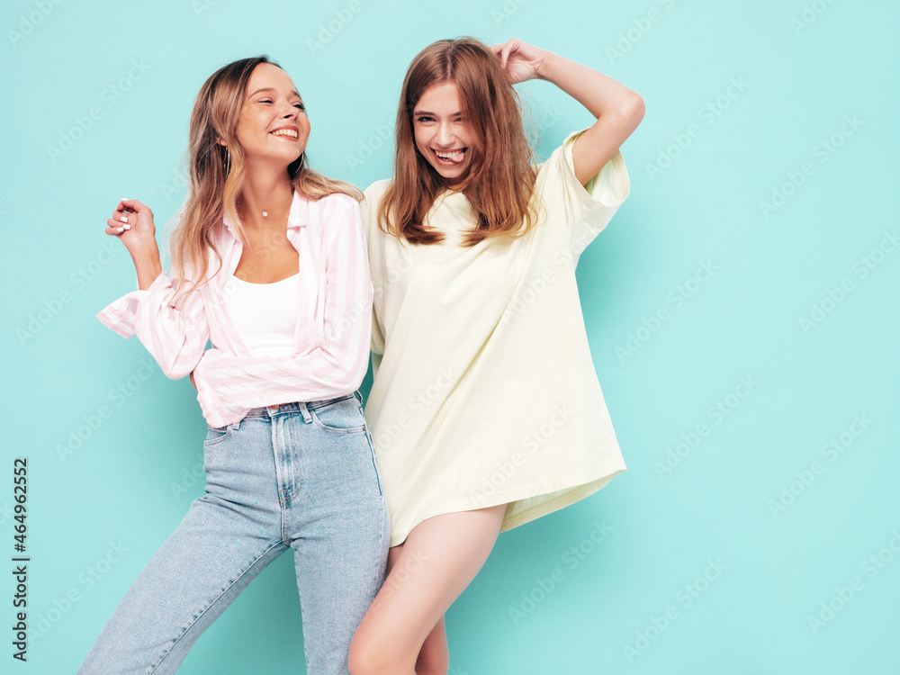 Two young beautiful smiling brunette hipster female in trendy summer clothes. Sexy carefree women posing near blue wall. Positive models having fun. Cheerful and happy Two young beautiful smiling brunette hipster female in trendy summer clothes. Sexy carefree women posing near blue wall. Positive models having fun. Cheerful and happy