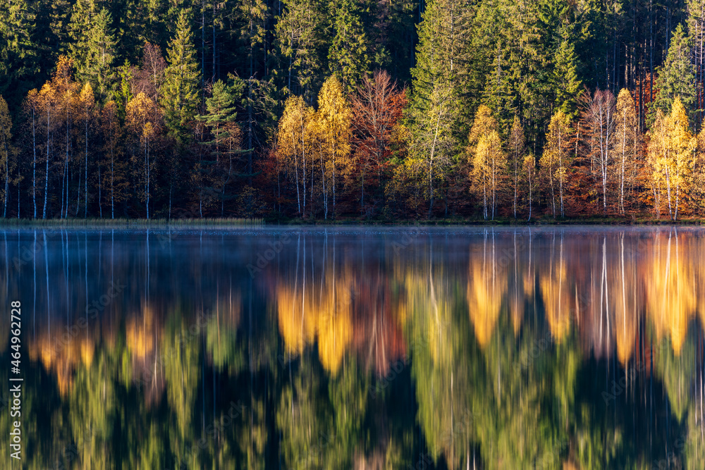 Idyllic autumn landscape with colorful green and yellow trees reflecting in the lake. Transylvania, Saint Anne Lake.