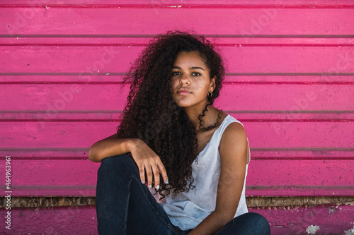 Portrait of a teenage Cuban girl outside sitting in front of a pink wall, hispanic multiracial teenage woman closeup