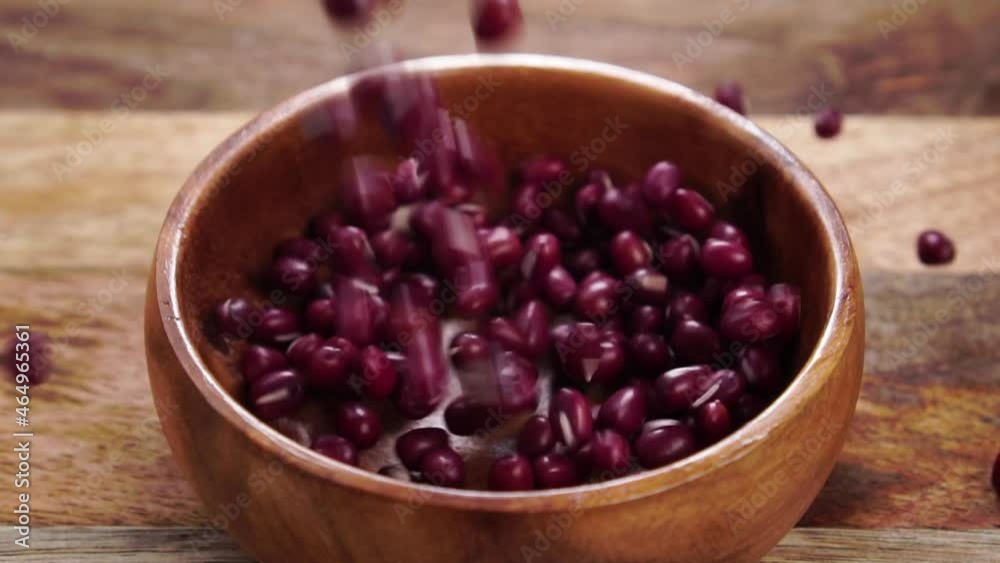 Red adzuki or azuki beans. Uncooked legumes fall into a rustic wooden bowl on a wood textured surface. Slow motion. Close up. Traditional Japanese food. Vigna angularis Red adzuki or azuki beans. Uncooked legumes fall into a rustic wooden bowl on a wood textured surface. Slow motion. Close up. Traditional Japanese food. Vigna angularis