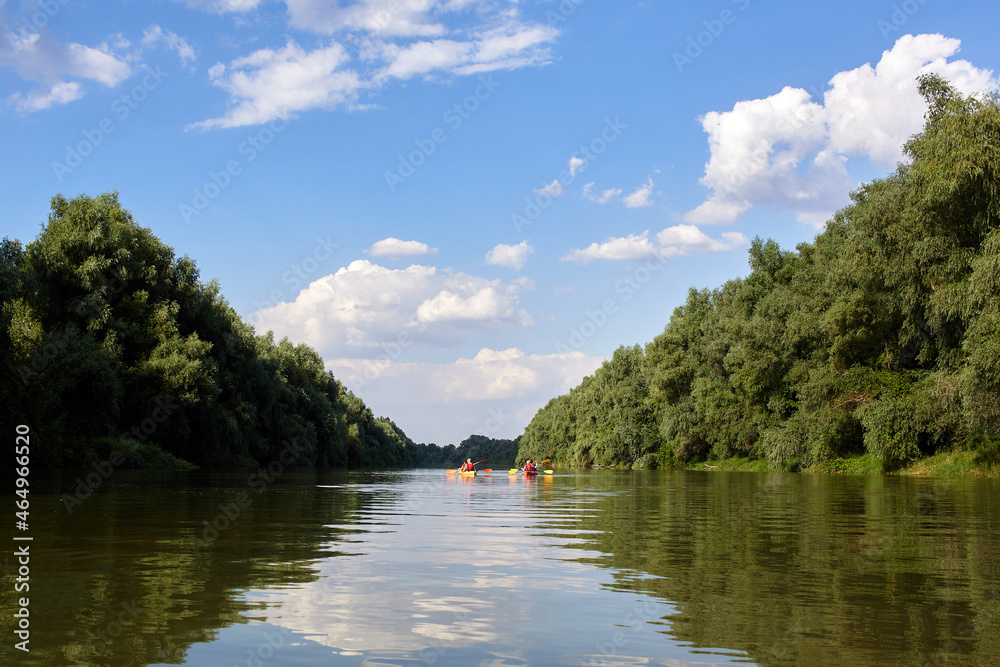 Landscape view of people in kyak on summer river near green trees. Peacefull nature scene