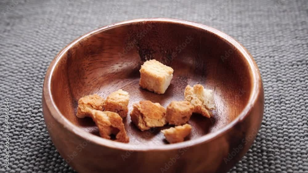 Bread baked rusks cubes fall into a rustic wooden bowl in slow motion on a rough jute surface. Close up Bread baked rusks cubes fall into a rustic wooden bowl in slow motion on a rough jute surface. Close up