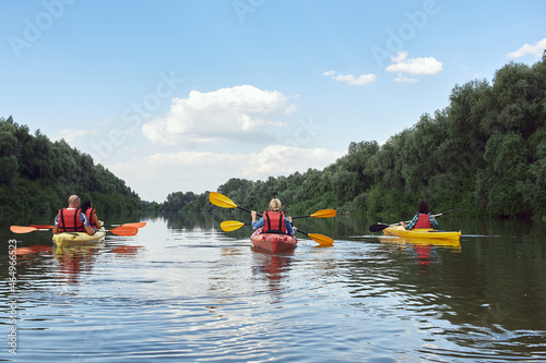 Friends kayaking in summer river against trees and blue sky