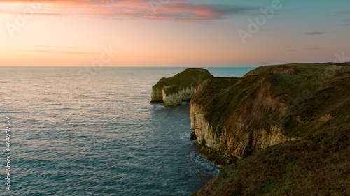 Sunrise over sea and eroded chalk cliffs under bright sky along coastline. Flamborough, UK.