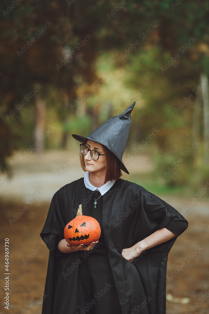 Halloween witch. Portrait of a girl in a hat and a witch costume with a pumpkin in the forest. Ready for the holiday