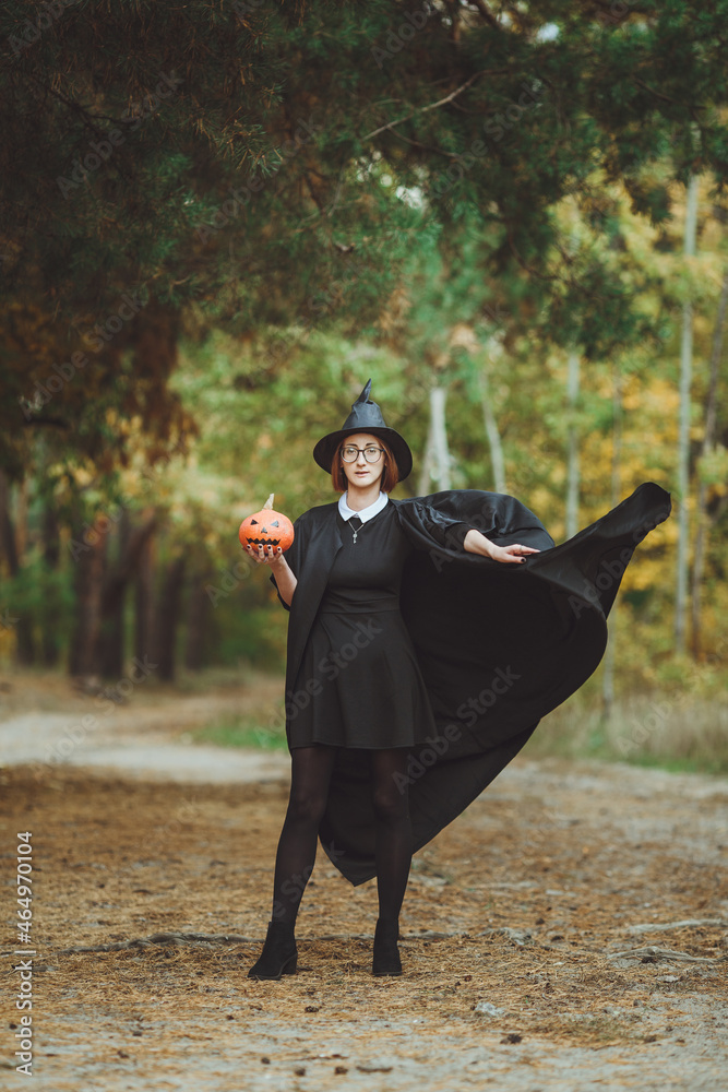 Halloween witch. Portrait of a girl in a hat and a witch costume with a pumpkin in the forest. Ready for the holiday