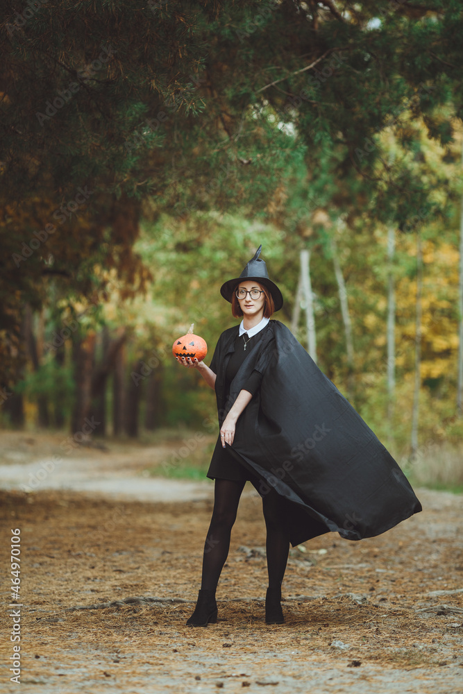 Halloween witch. Portrait of a girl in a hat and a witch costume with a pumpkin in the forest. Ready for the holiday