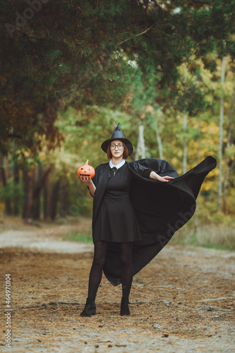 Obraz na płótnie Halloween witch. Portrait of a girl in a hat and a witch costume with a pumpkin in the forest. Ready for the holiday