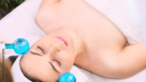 Calm patient woman undergoing the cosmetic facial massage procedures for rejuvenation skin face and doctor using cosmetic instruments, ice balls massage