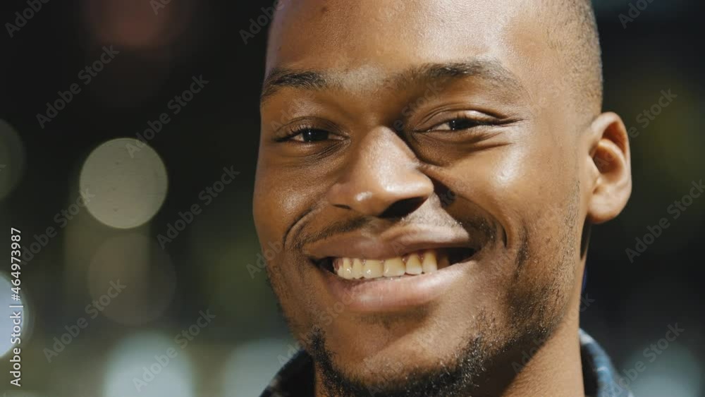 Male happy portrait african american young millennial satisfied man stands in city in evening town lights background looking at camera smiling toothy waving head in agreement answering yes close up Male happy portrait african american young millennial satisfied man stands in city in evening town lights background looking at camera smiling toothy waving head in agreement answering yes close up