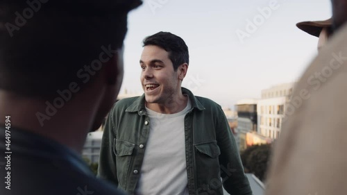 Adult Caucasian Male socializing with a diverse group of friends at rooftop party. Chatting lightheartedly at sunset. High quality image. photo