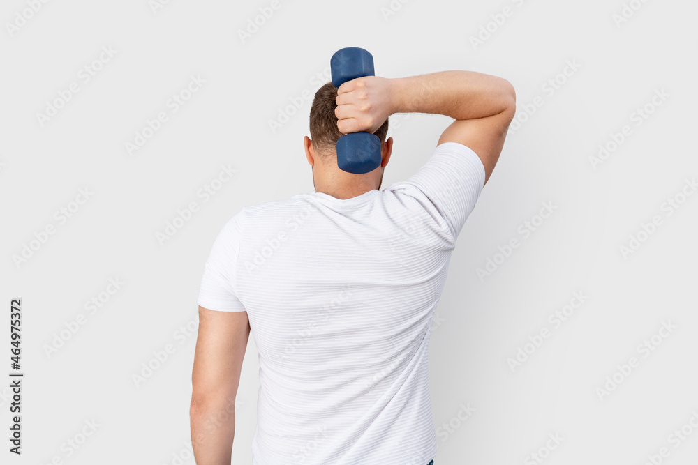 Young man with white t-shirt exercises with dumbbell against grey wall Young man with white t-shirt exercises with dumbbell against grey wall