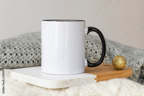 White ceramic coffee cup with black handle mockup on cozy winter background with warm sweaters and copy space for your design. Standard 11 oz mug with golden handle for imprint branding and souvenirs
