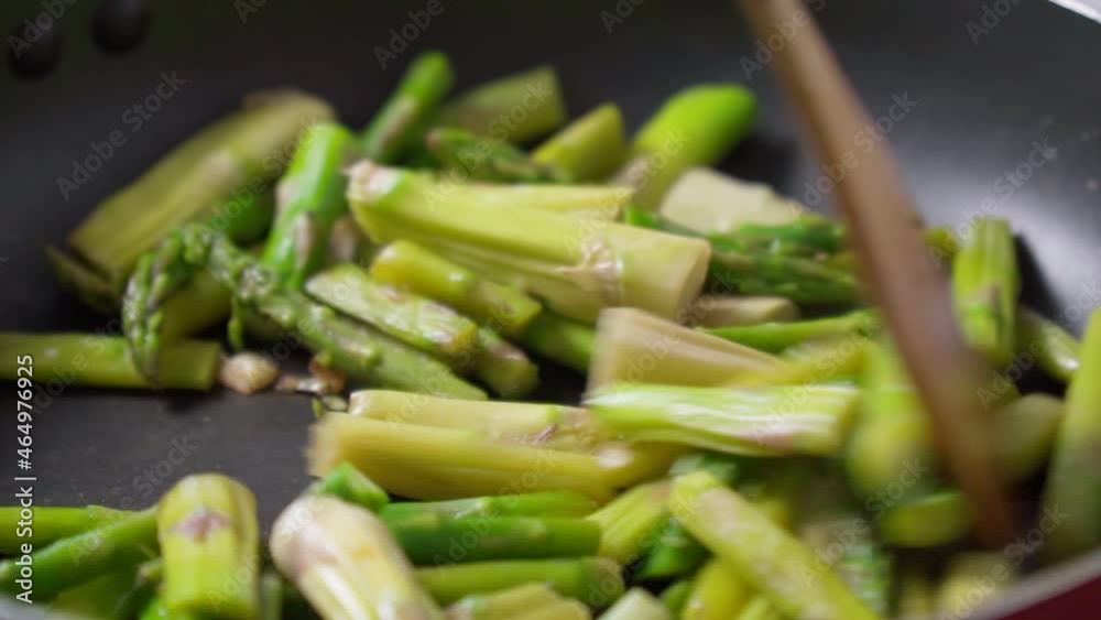 Green asparagus stalks are fried in a large frying pan. Close-up. Selective focus Green asparagus stalks are fried in a large frying pan. Close-up. Selective focus