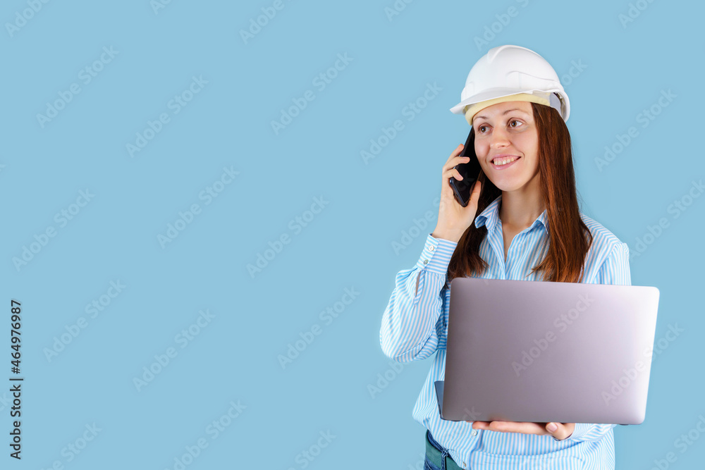 A female engineer in a hardcat with a laptop on a blue background, calling on a mobile phone. Copyspace A female engineer in a hardcat with a laptop on a blue background, calling on a mobile phone. Copyspace