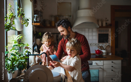Mature father with two small children washing dishes indoors at home, daily chores concept. photo