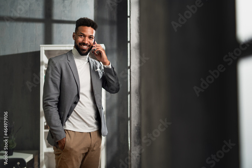 Happy young african american businessman with martphone indoors in office, looking at camera.